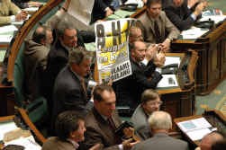 Terwijl Guy Verhofstadt (rechts) een staande ovatie krijgt van de paarse kamerleden, haalt Gerolf Annemans (Vlaams Belang) een B-H-V-affiche boven.