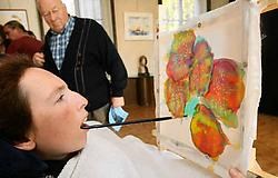Brenda demonstreert hoe ze het penseel hanteert <br>met de mond.<br> Eddy Van Ranst