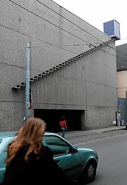 De enorme betonmuur in de Sint-Michielsstraat, tussen de Sint-Michielskerk en de Poel, was al direct na de bouw voor velen een visuele 'steen des aanstoots'. Zelfs ingrepen van kunstenaars konden de pijn niet verzachten.gia <br>