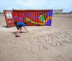 Andrew van der Merwe kalligrafeert het getijdegedicht van David Van Reybrouck in het zand.rr <br>