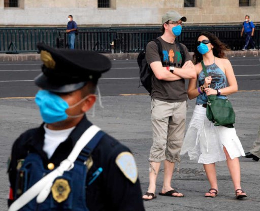 Buitenlandse toeristen op het Zocalo-plein in Mexico-Stad, mét mondmasker, net zoals de Mexicaanse politieagent.ap