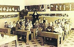 Een klas van de school met de oude zitbanken, een zandbak op de voorgrond en een zuster die surveilleert. jdv