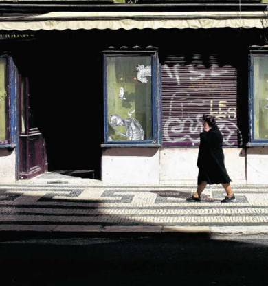 Een vrouw loopt voorbij een gesloten winkel de benedenstad van Lissabon.ap