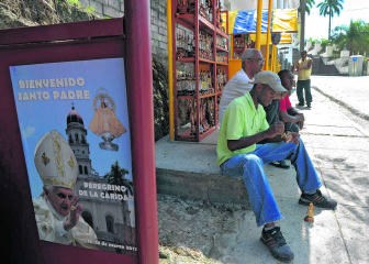 Een ambachtsman in El Cobre werkt aan een religieus beeldje. Naast hem hangt een affiche die het pausbezoek aankondigt.afp