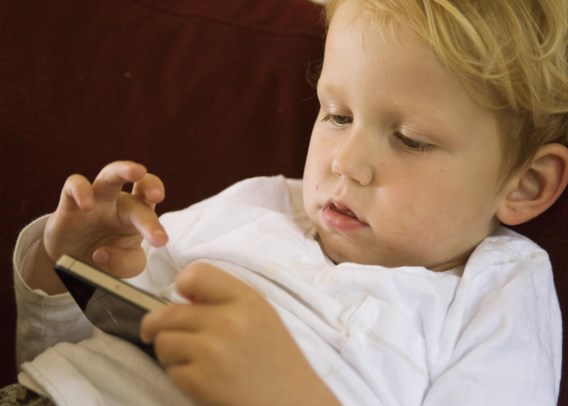 Een 2,5 jaar oud jongetje speelt geboeid met een iPhone. 