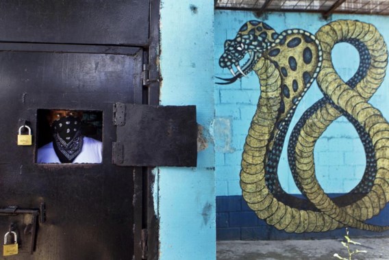 Een gemaskerd lid van de M 18-bende tuurt door het luikje van zijn cel in de gevangenis van San Pedro Sula.