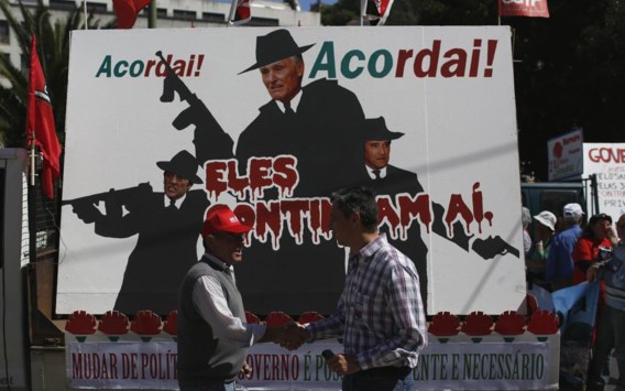 In een 1 mei-optocht in Lissabon voeren betogers een affiche mee waarop premier Passos Coelho (rechts), president Anibal Cavaco Silva (midden) and vicepremier Paulo Portas worden afgeschilderd als gangsters.