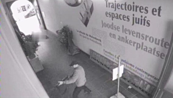 De moordenaar schiet met zijn machinegeweer een salvo af in het museum. Vlak bij de uitgang liggen al twee doden.