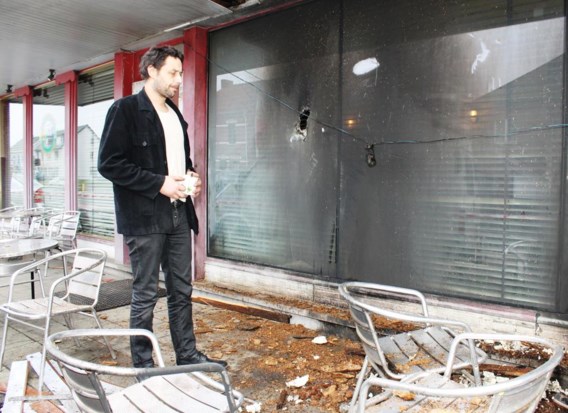 Cafébaas Bert Kindermans aan het raam van zijn café, waar duidelijk de schade van de brandbom te zien is. 