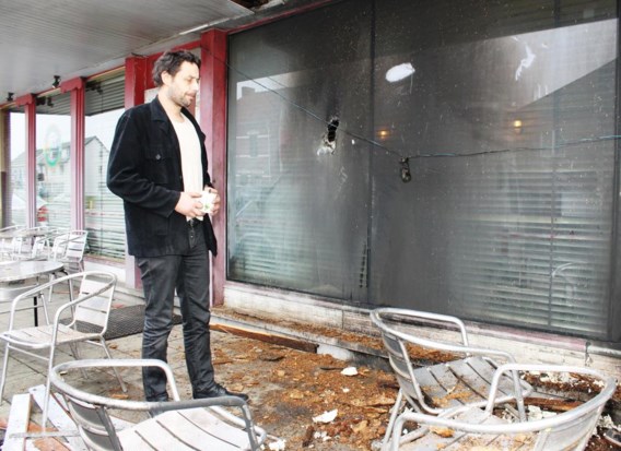 Cafébaas Bert Kindermans aan het raam van zijn café, waar duidelijk de schade van de brandbom te zien is.
