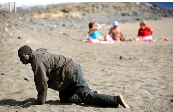Een vluchteling kruipt over het strand van het Spaanse Gran Tarajal nadat hij is aangekomen met een bootje.