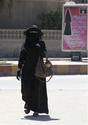 Een gesluierde vrouw in de straten van Raqqa doet wat de kledijvoorschriften van ISIS haar op het publiciteitsbord dicteren.