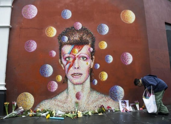 Een man legt bloemen neer bij een muurschildering van Bowie in Brixton.