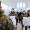December 2020: Hongaarse soldaten dragen in een ziekenhuis in Boedapest dozen met de eerste exemplaren van het ??????????Pfizer-vaccin binnen. Hongarije is een van de tien landen die vinden dat de contracten met de farmabedrijven grondig herzien en desnoods opgezegd moeten worden. 